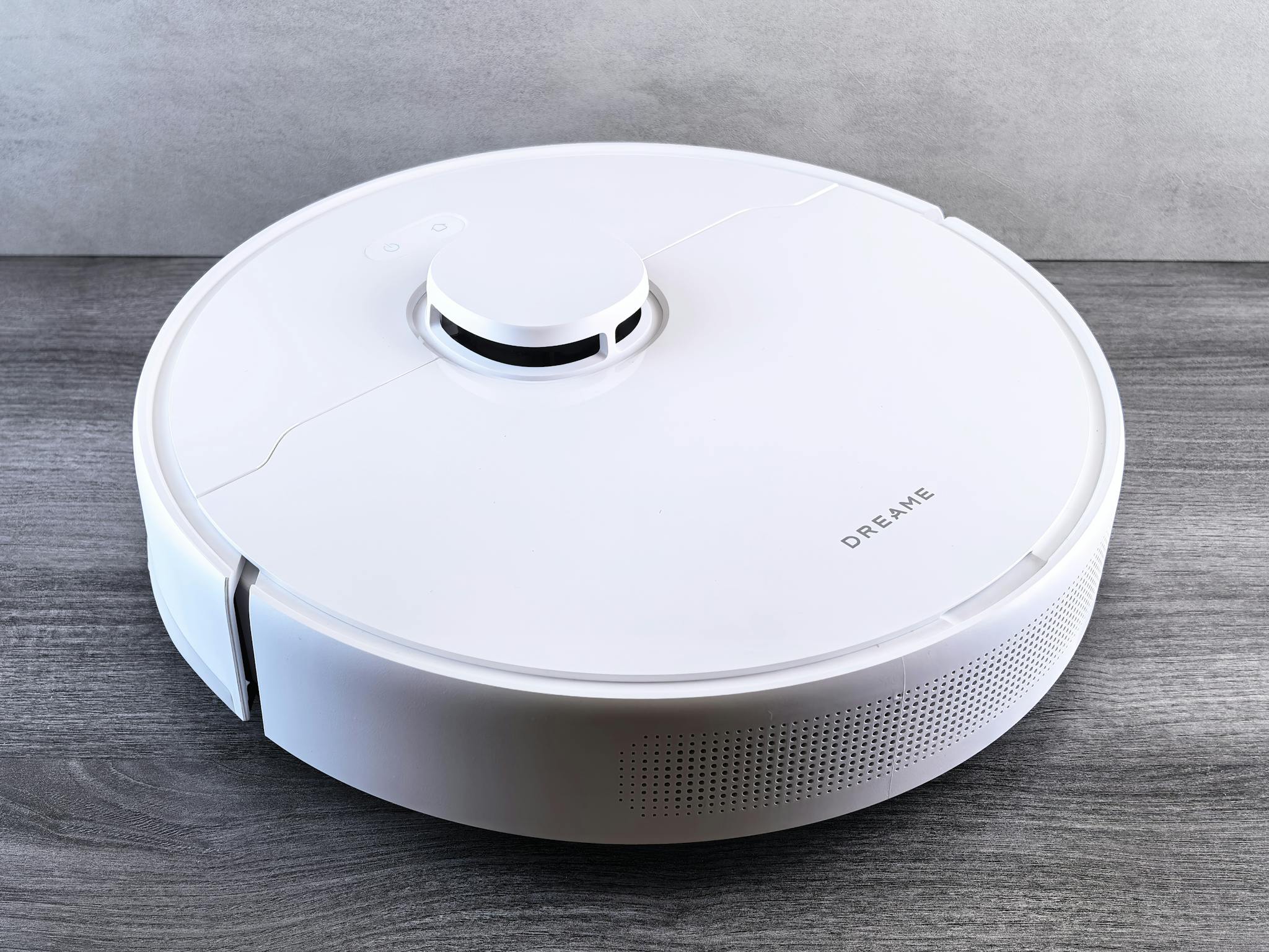 High-angle view of a sleek white robotic vacuum cleaner on a wooden floor, perfect for smart home setups.